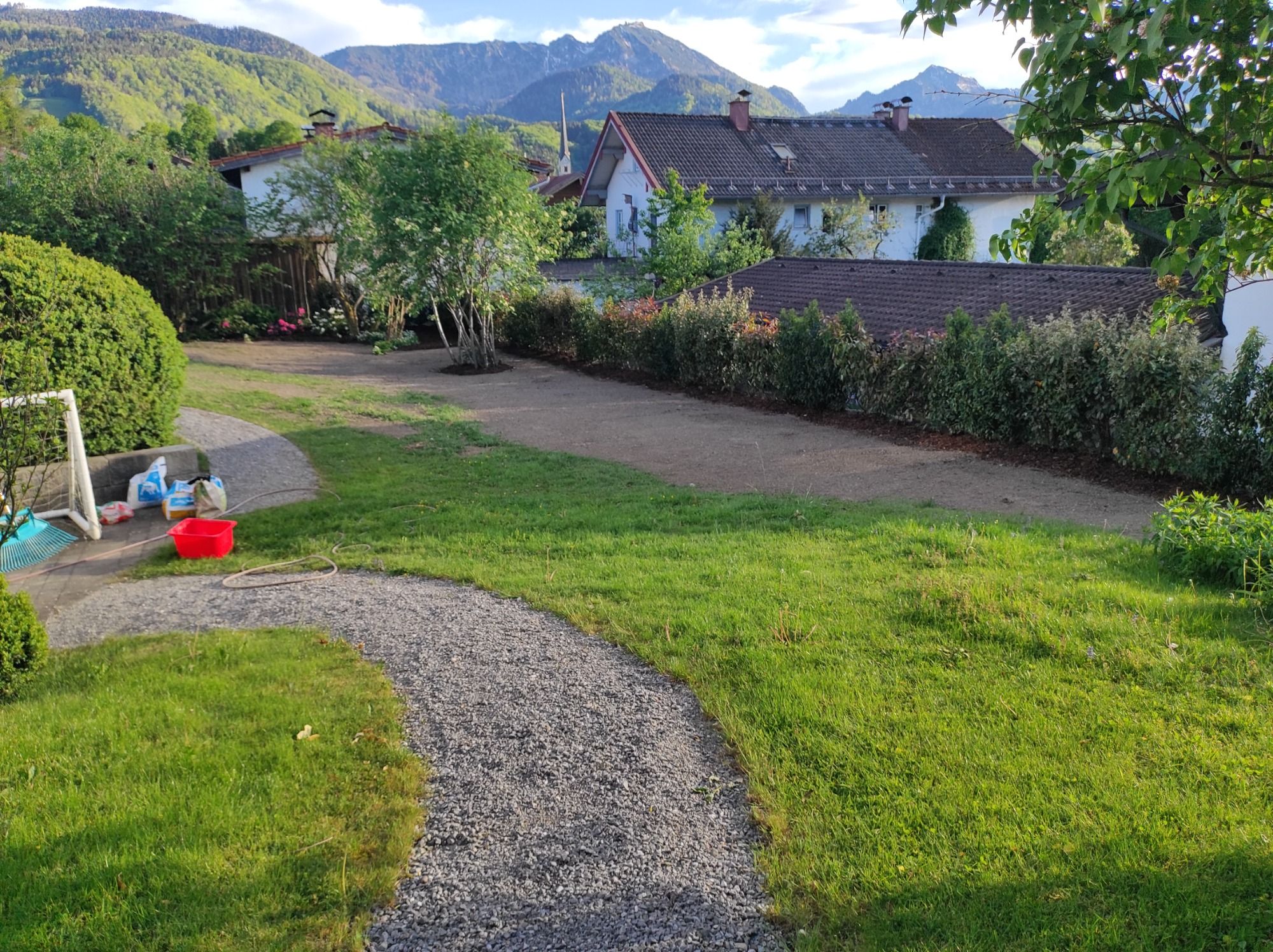 Neu gestalteter Garten mit geschwungenem Kiesweg vor Bergkulisse.