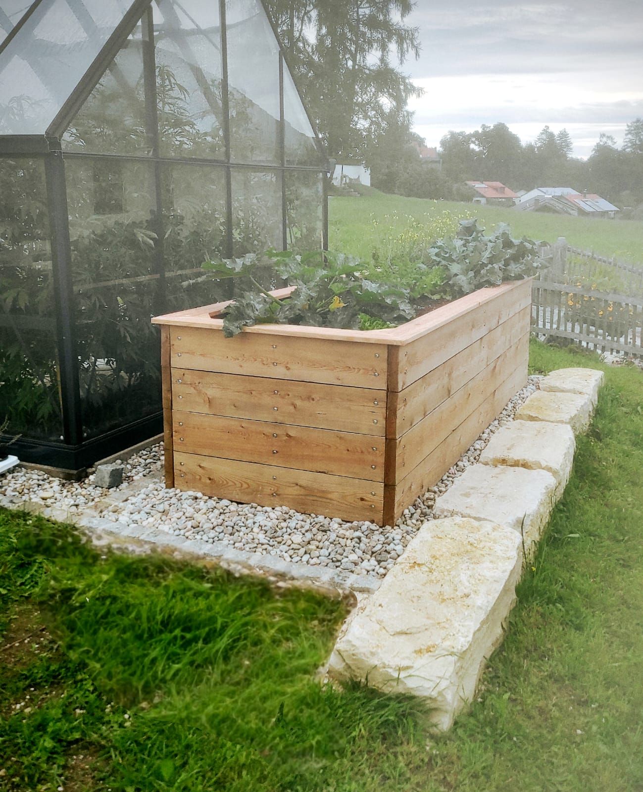 Selbst gebautes Holz-Hochbeet neben einem Gewächshaus.